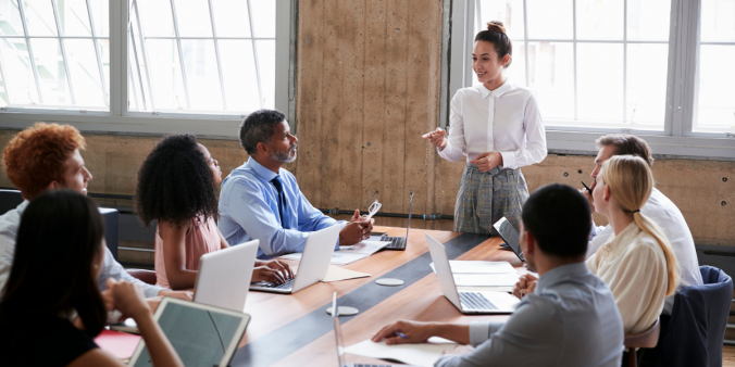 Eight people sitting around a board room table discussing.