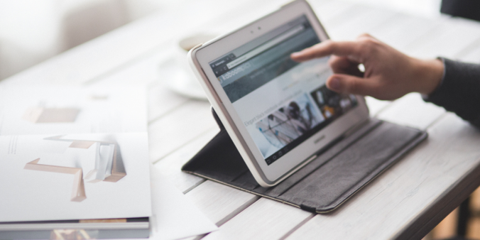 Individual pointing at an ipad laying on a wooden desk.